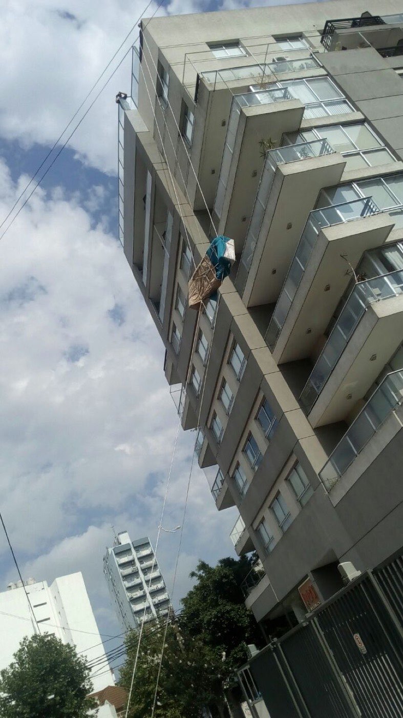 Mueble embalado descendiendo por la fachada de un edificio sujeto con sogas